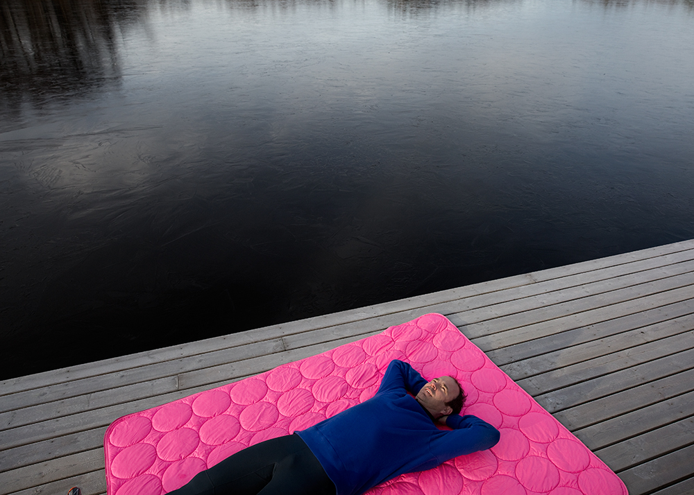 a man lying on a pink mat on a dock near water