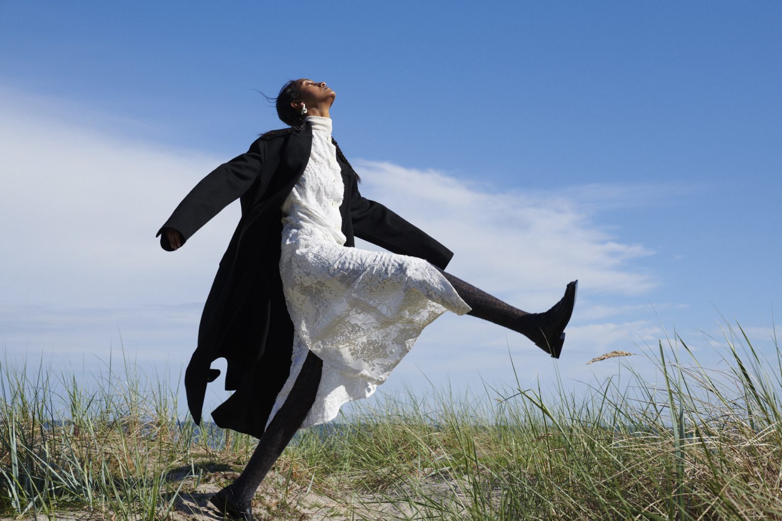 a woman in a white dress and black coat jumping in the air