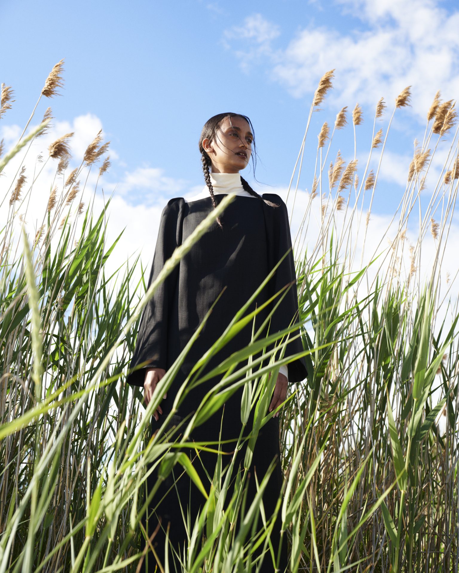 a woman in a black robe standing in tall grass