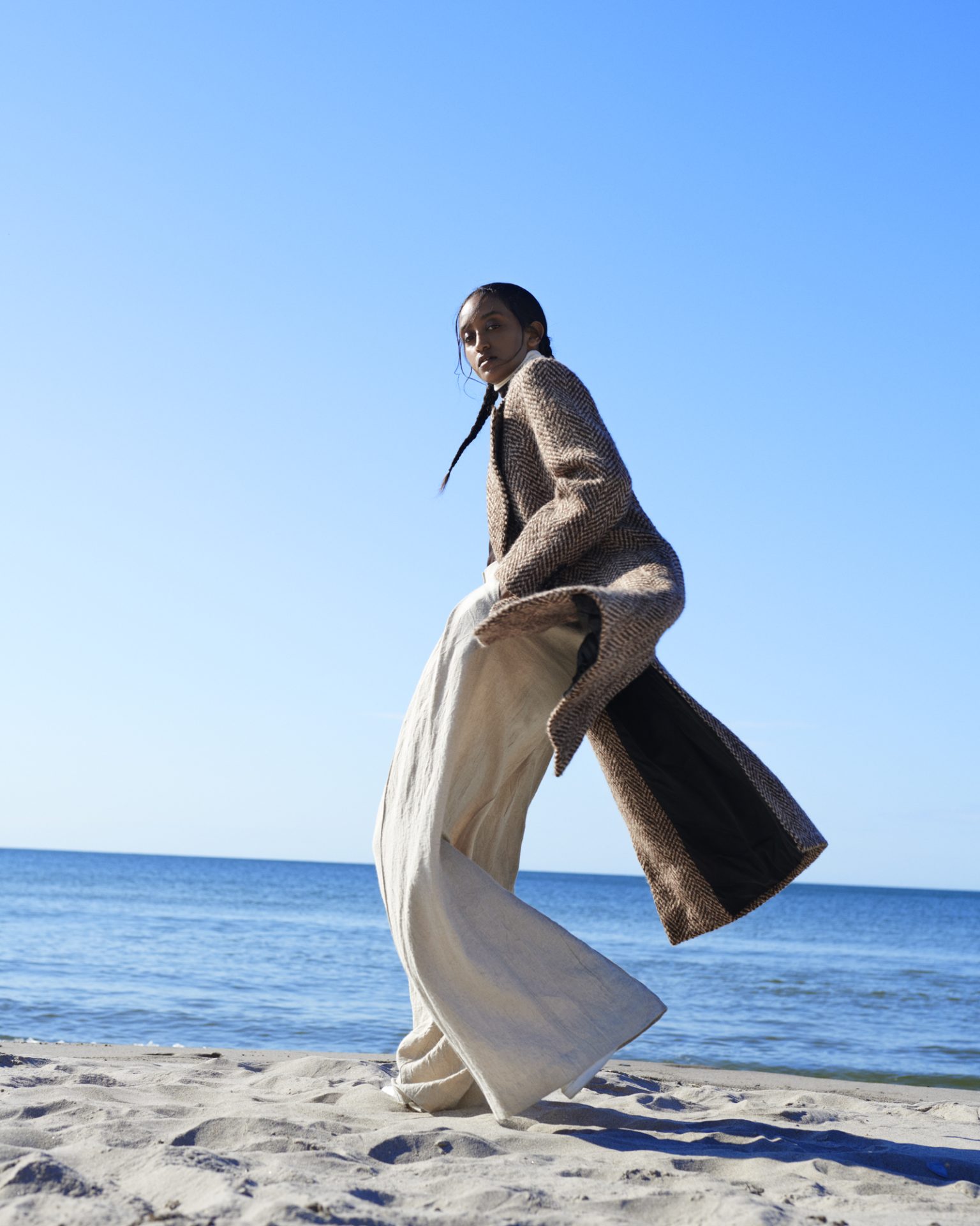 a woman in a long coat on a beach