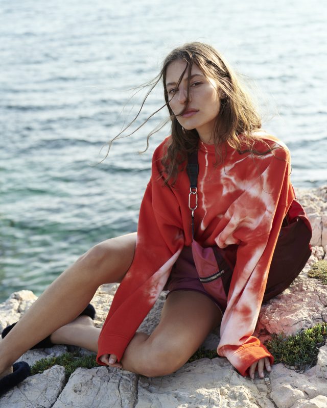 a woman sitting on a rock by the water