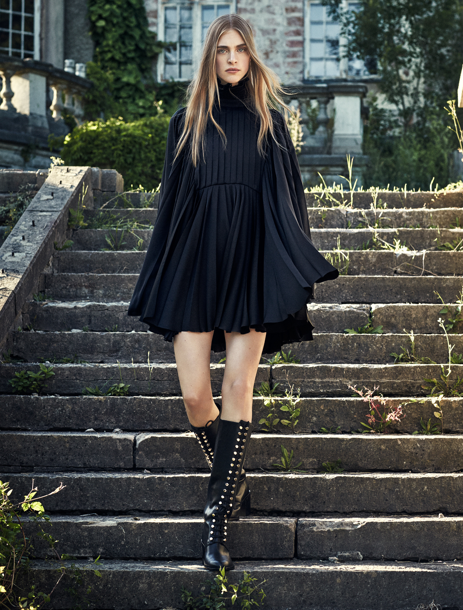 a woman in a black dress and boots walking up stairs