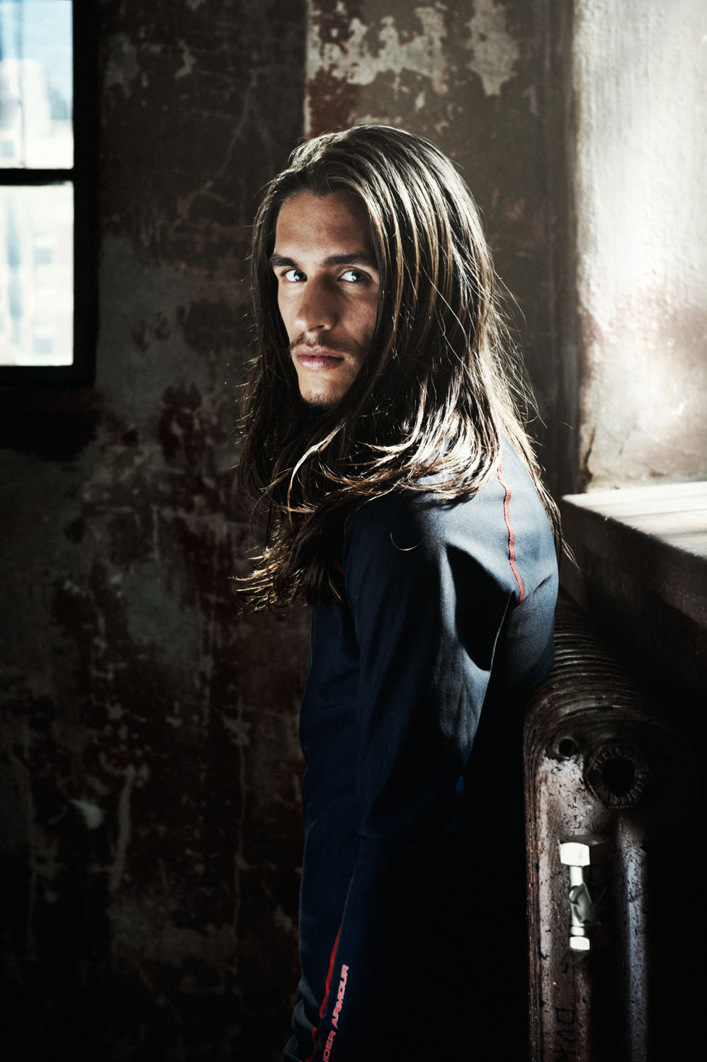 a man with long hair leaning against a radiator