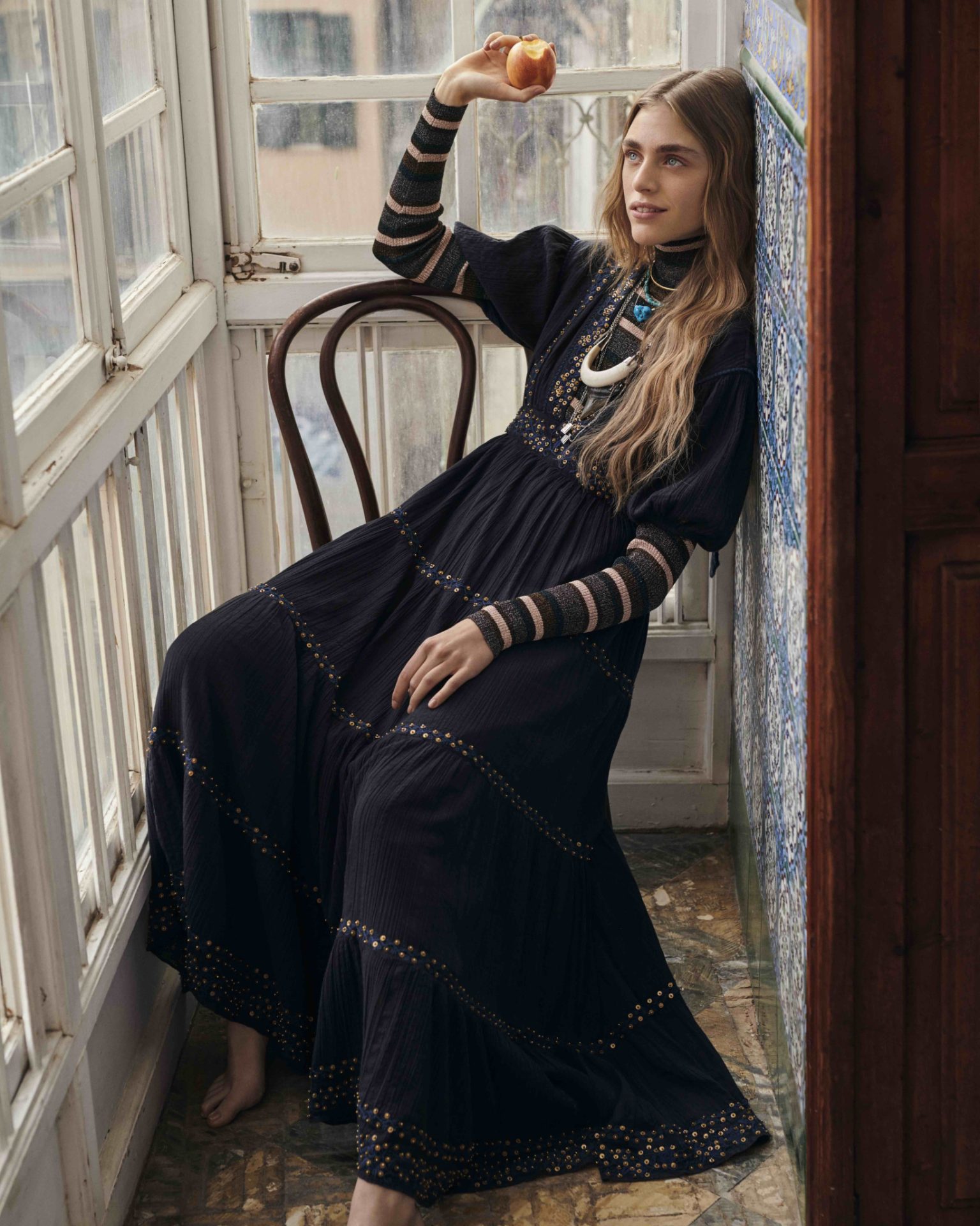 a woman in a long black dress leaning on a chair