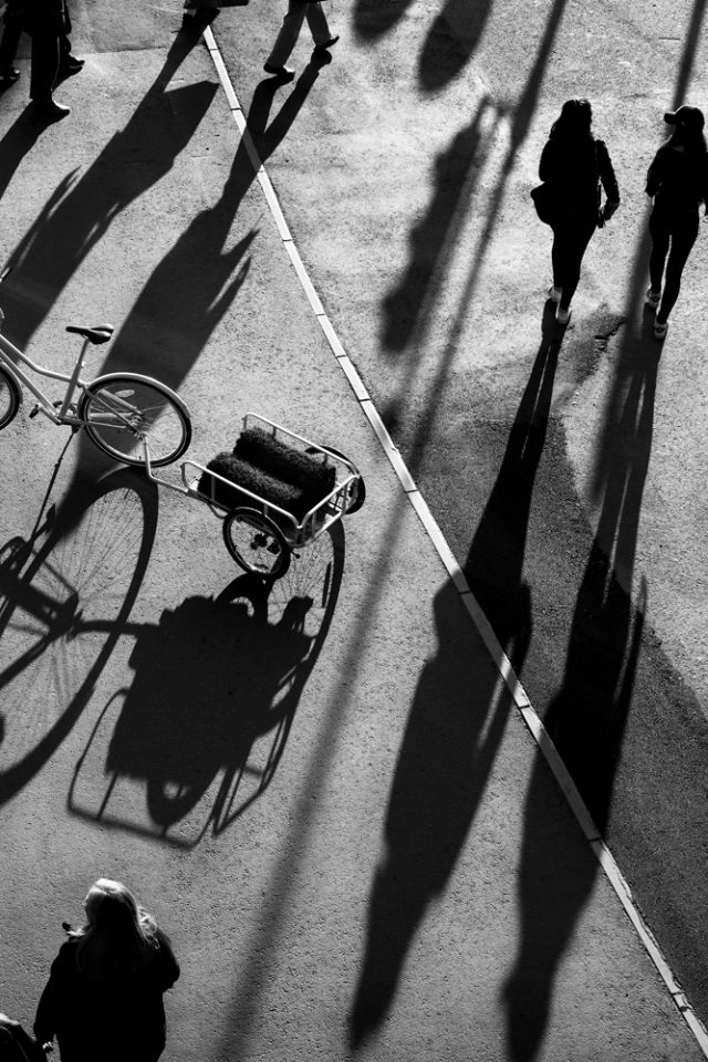 shadows of people walking on a sidewalk with a bicycle and a cart
