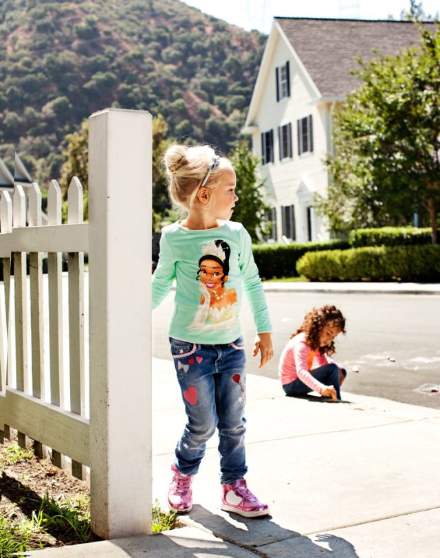 a girl standing on the sidewalk next to a white fence
