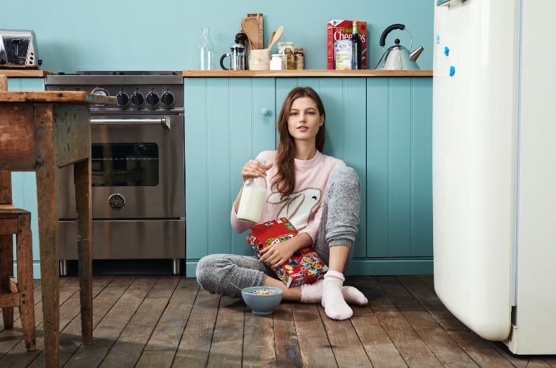 a woman sitting on the floor with a bowl and a box and a bottle of milk