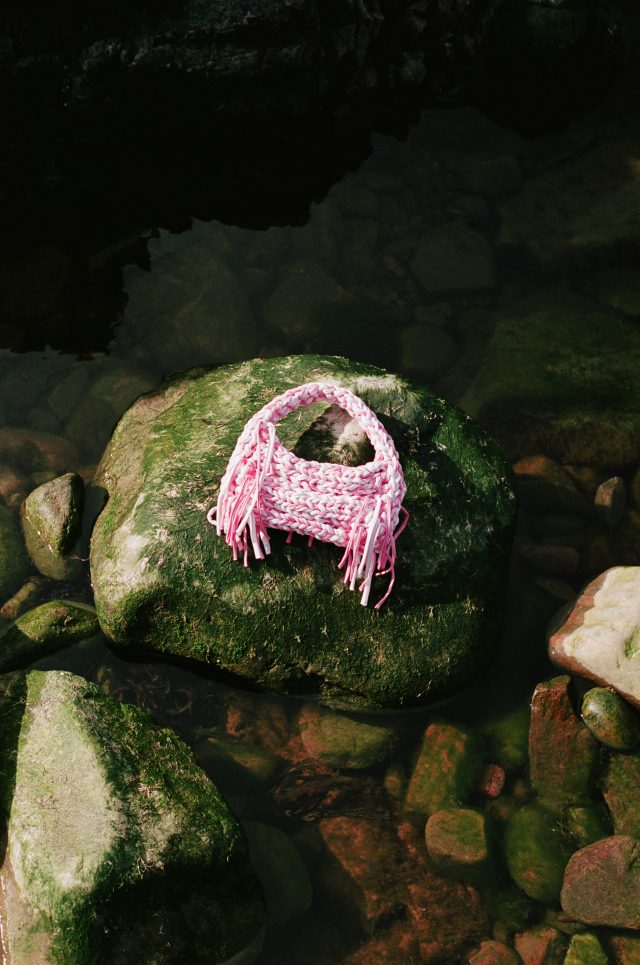 a pink knitted bag on a rock in water