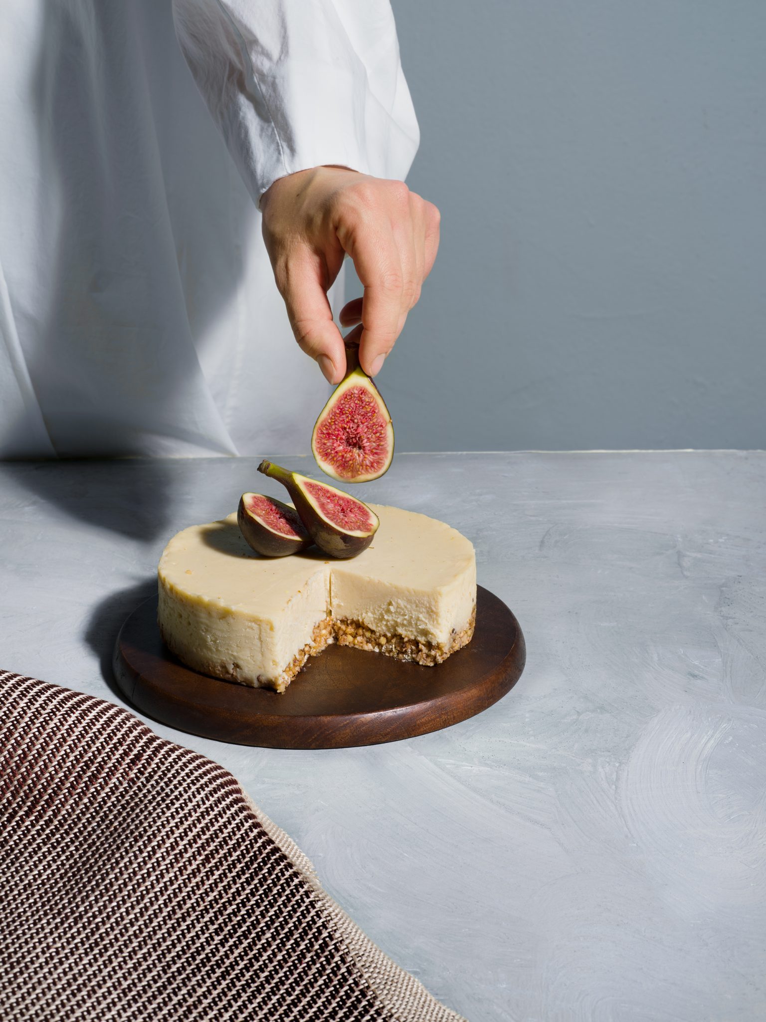 a person holding a fig over a cheesecake