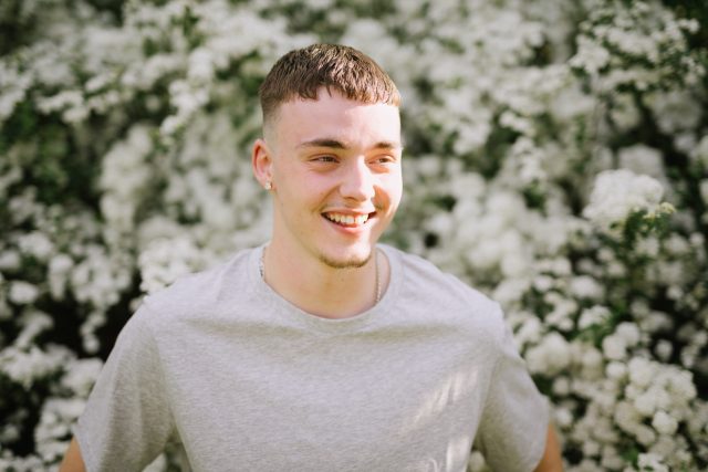 a man smiling in front of a bush of white flowers