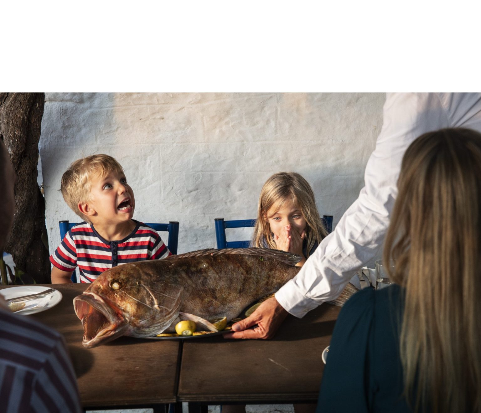 a group of kids sitting at a table with a large fish