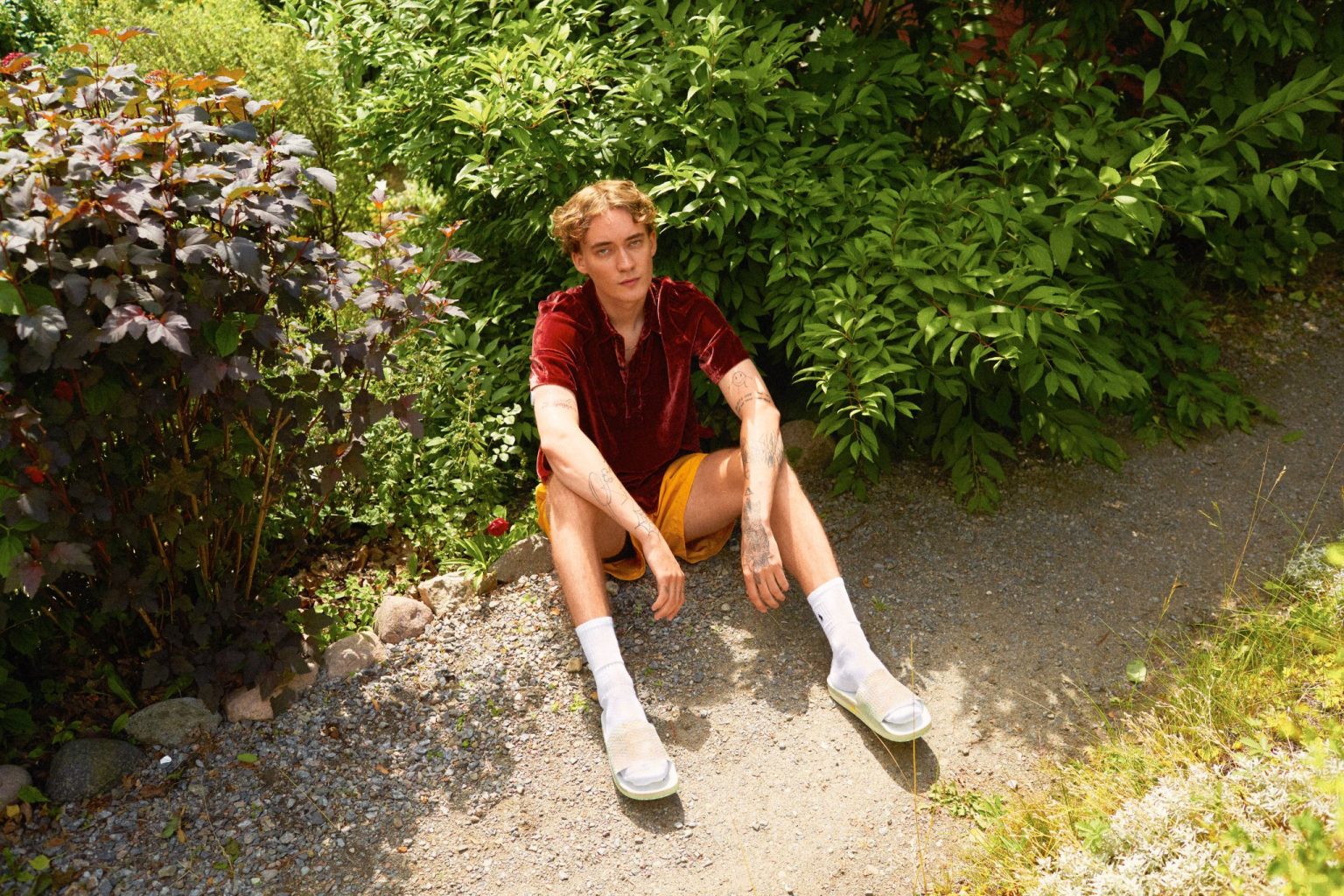 a man sitting on gravel near bushes