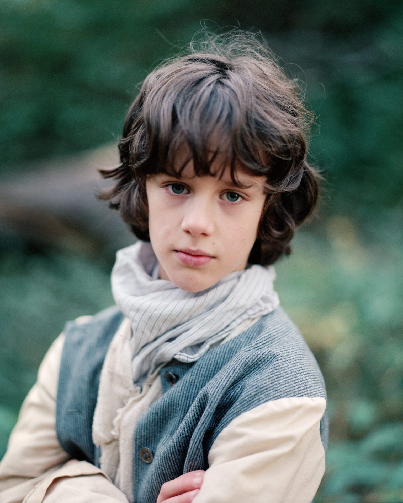 a boy with long hair wearing a scarf and vest