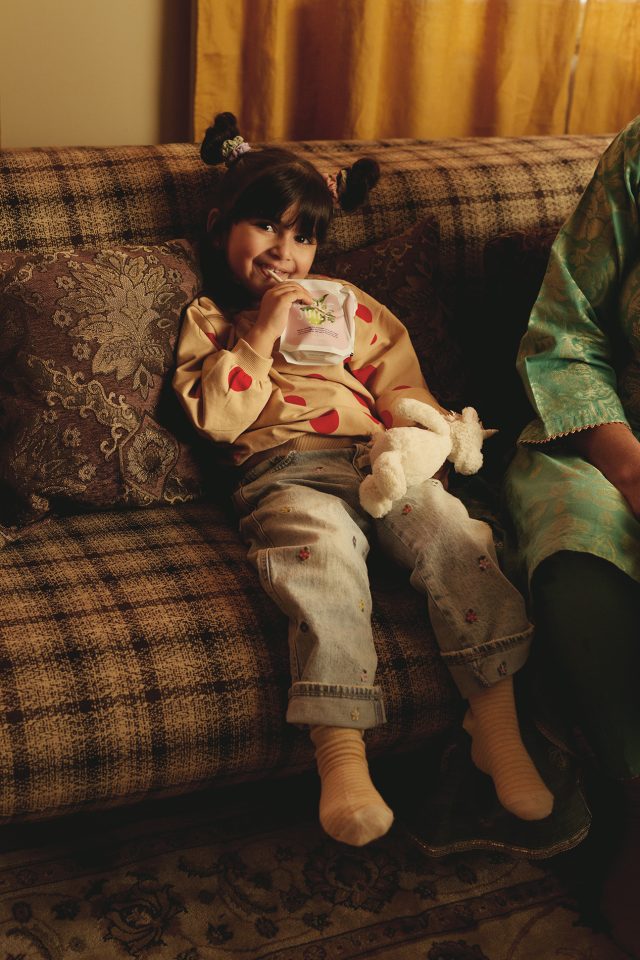 a girl sitting on a couch drinking from a plastic bag