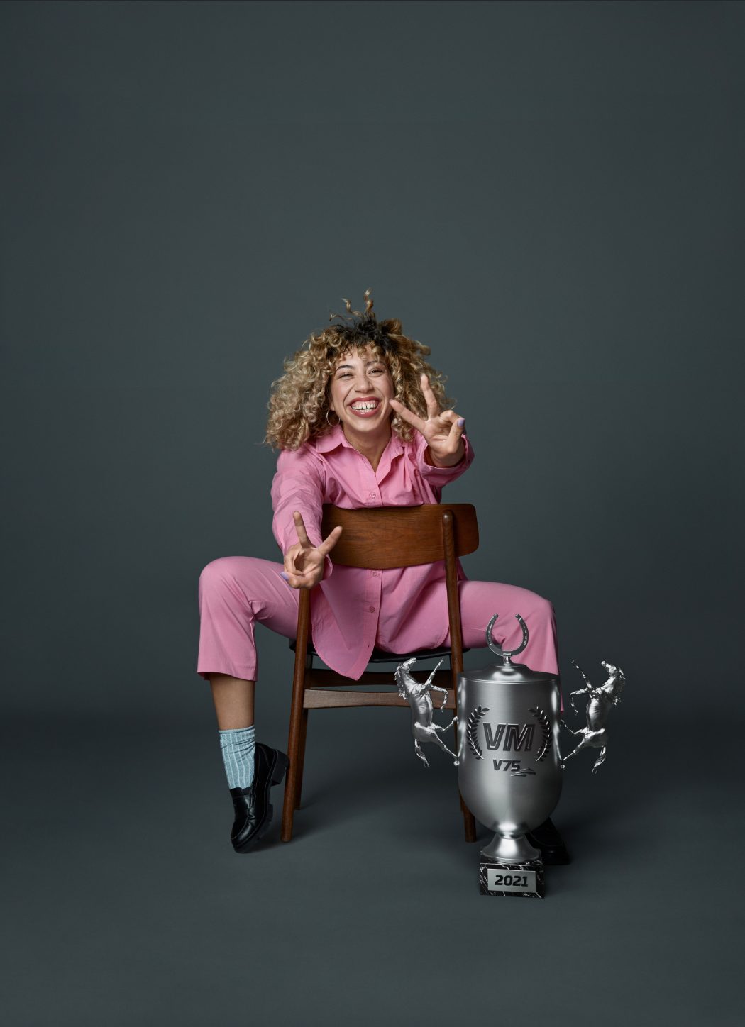 a woman sitting on a chair with a trophy and a peace sign