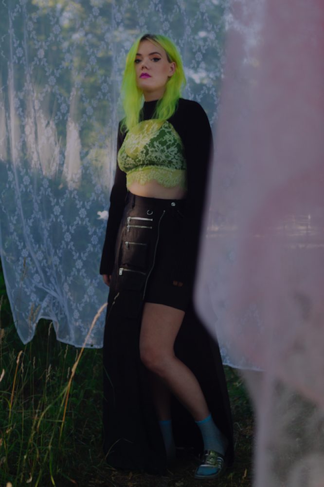 a woman with green hair standing in front of a curtain