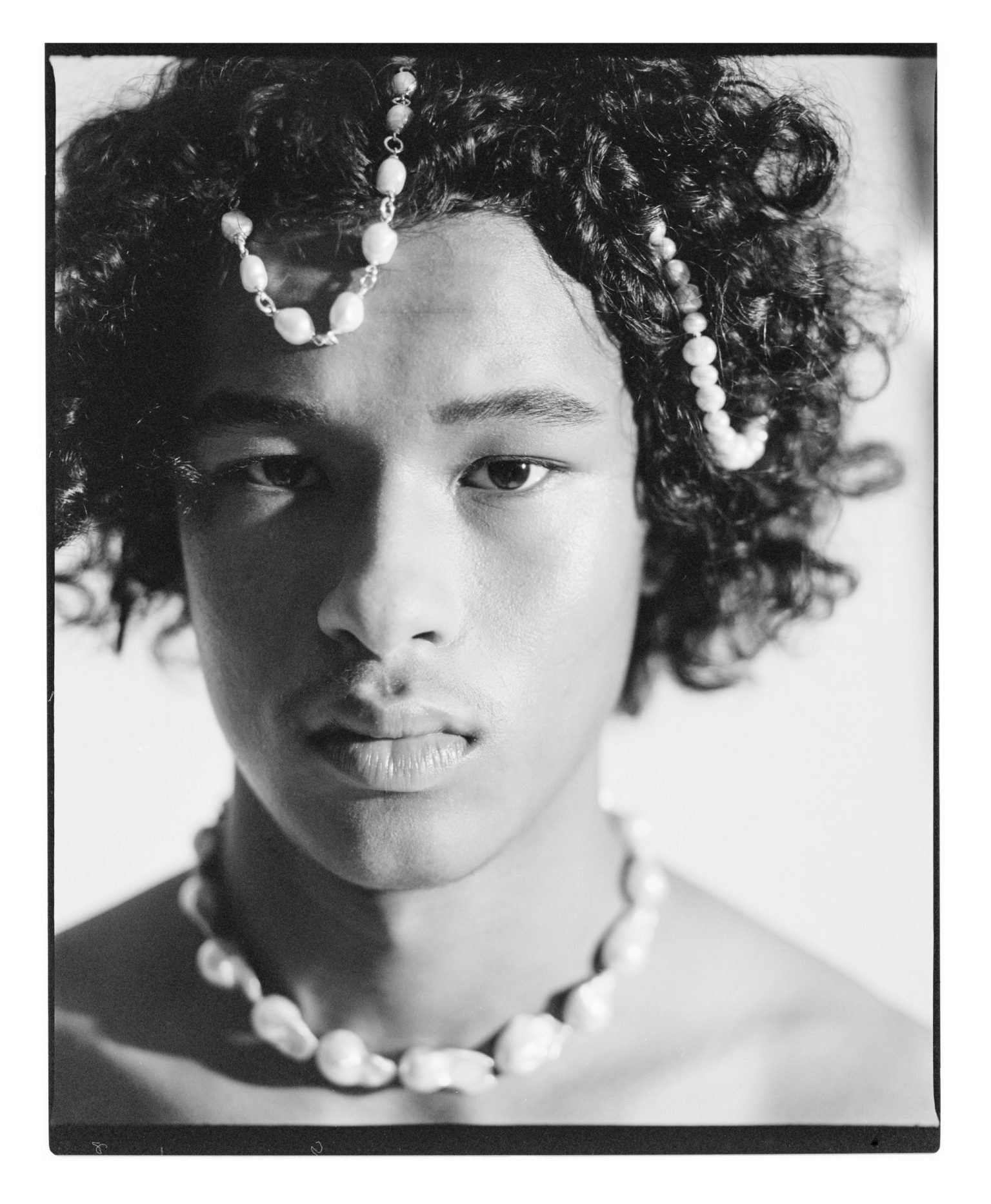 a man with curly hair and pearl necklace