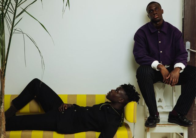 two men sitting on a yellow and white bench