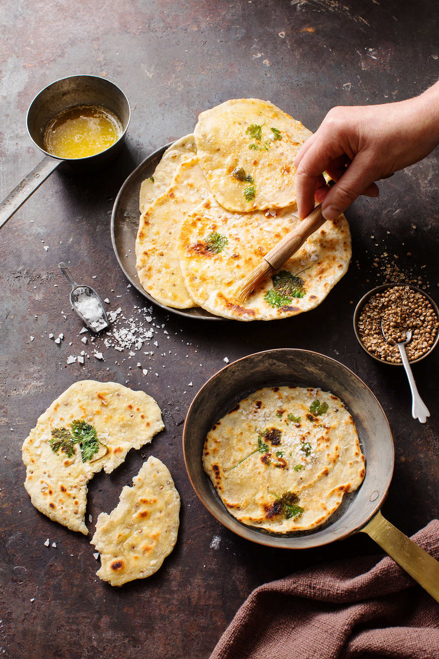 a hand holding a brush over a pan of flat bread