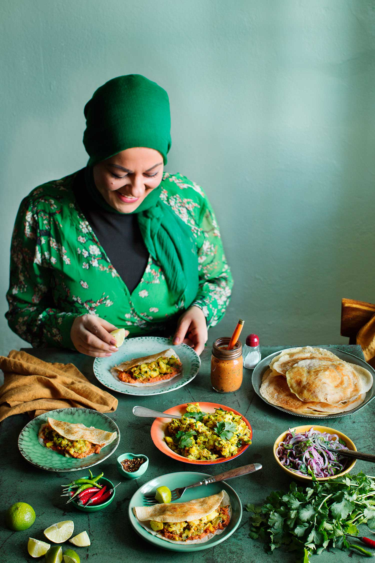a woman in a green shirt sitting at a table with plates of food