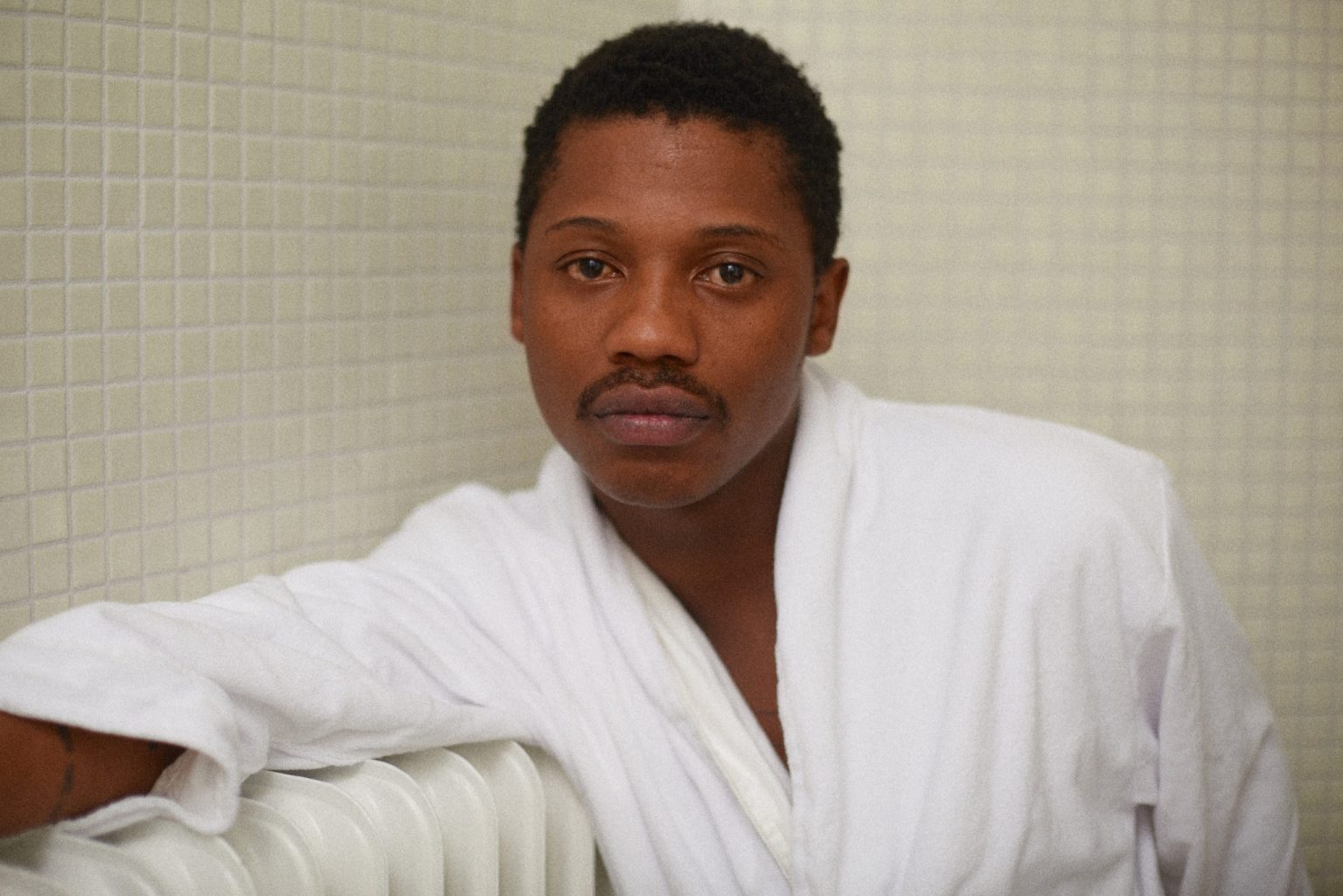 a man in a white robe leaning on a heater