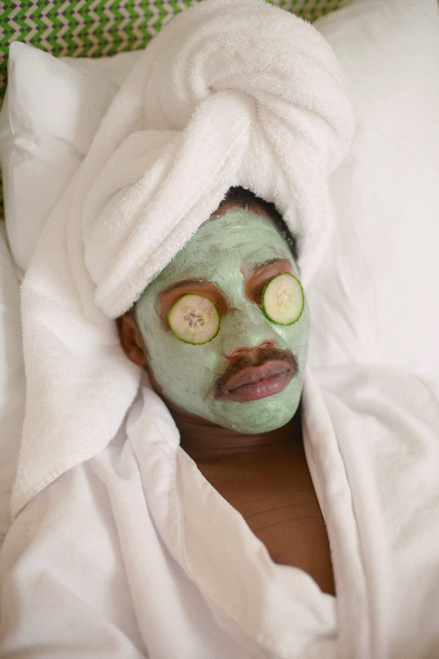 a man with a facial mask and cucumbers on his face