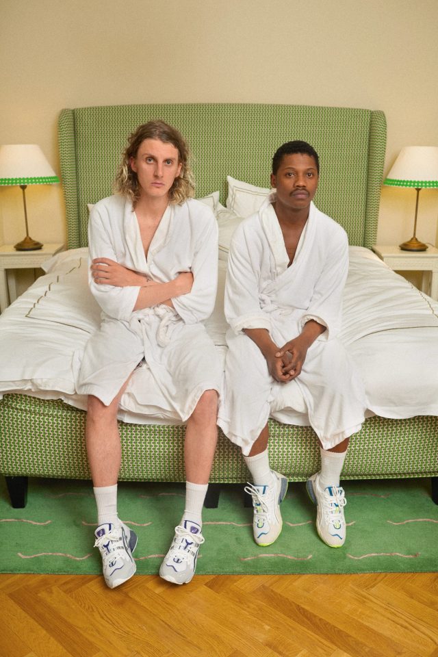 two men in white robes sitting on a bed