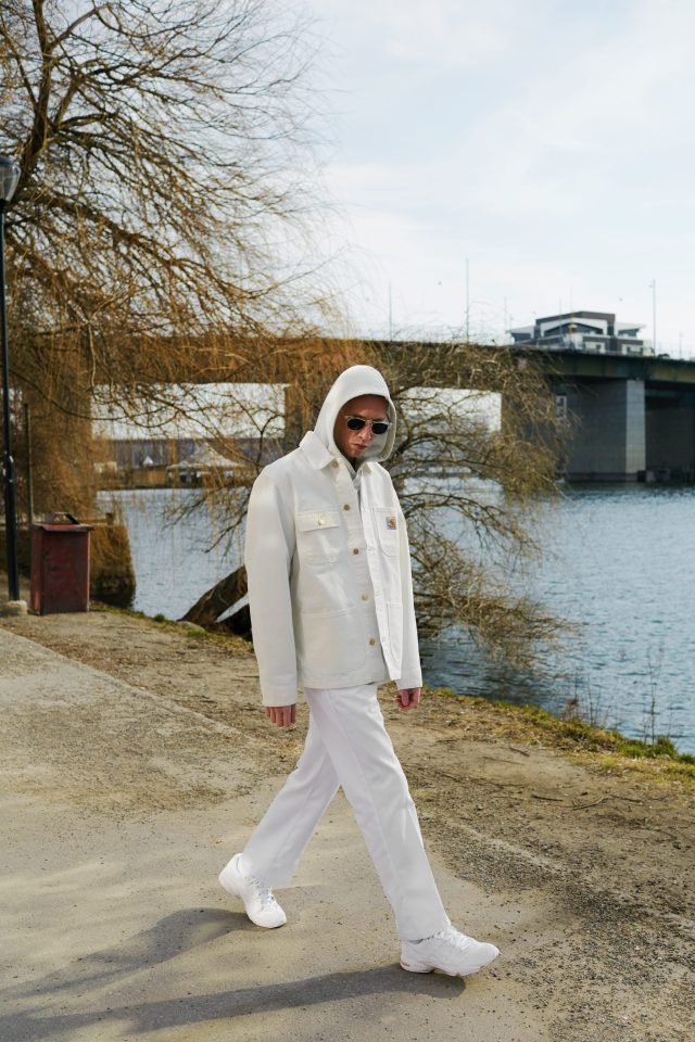 a man wearing white clothes and sunglasses walking on a path near water
