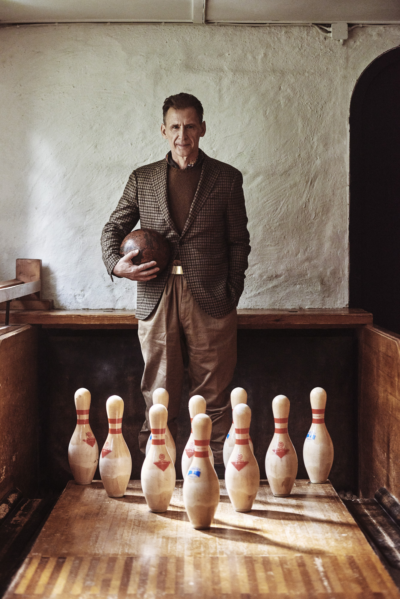 a man holding a ball and standing in front of a row of skittles