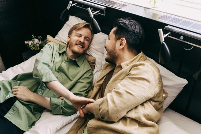 two men lying in bed holding hands