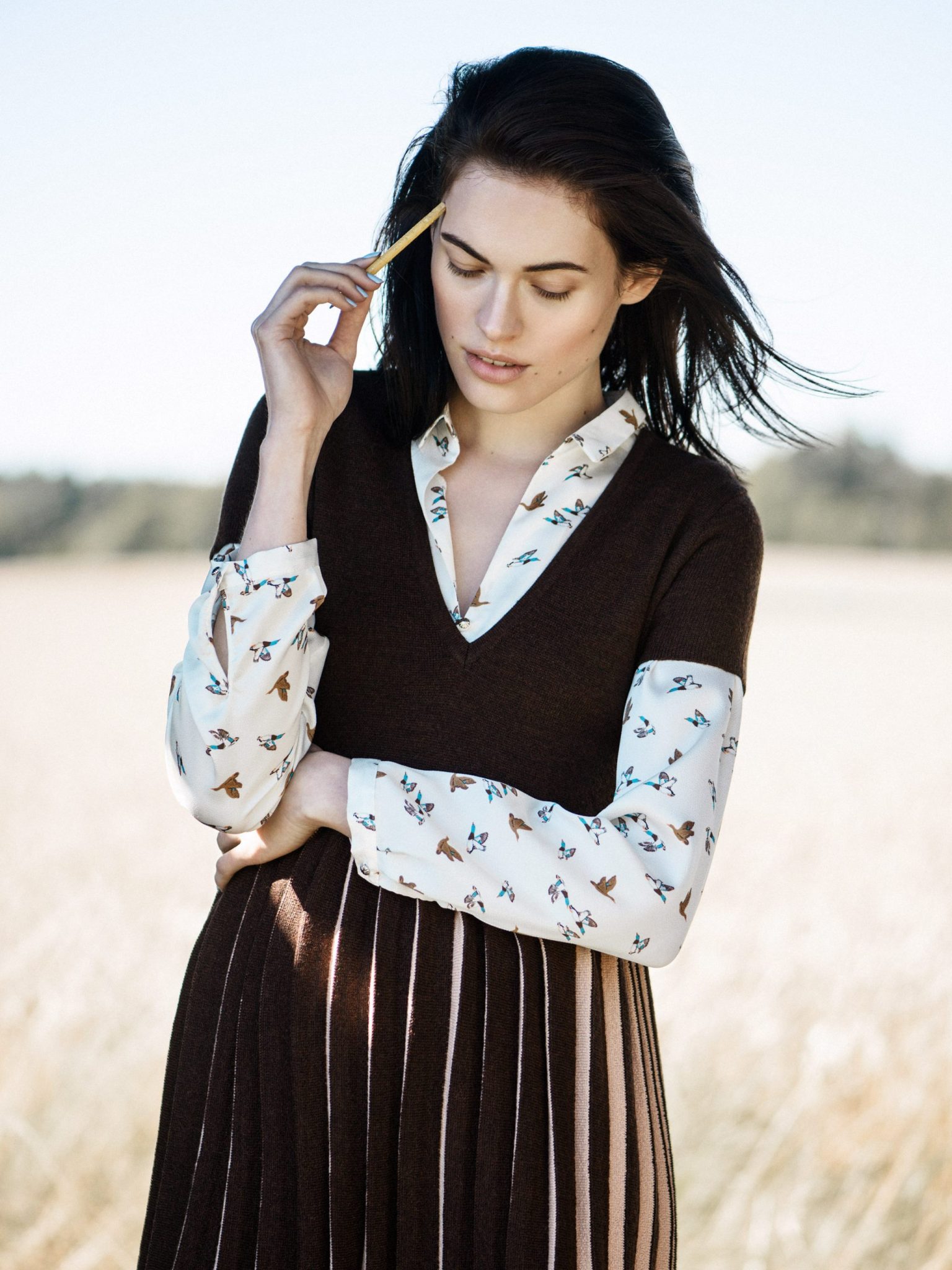 a woman in a brown sweater and skirt holding a stick
