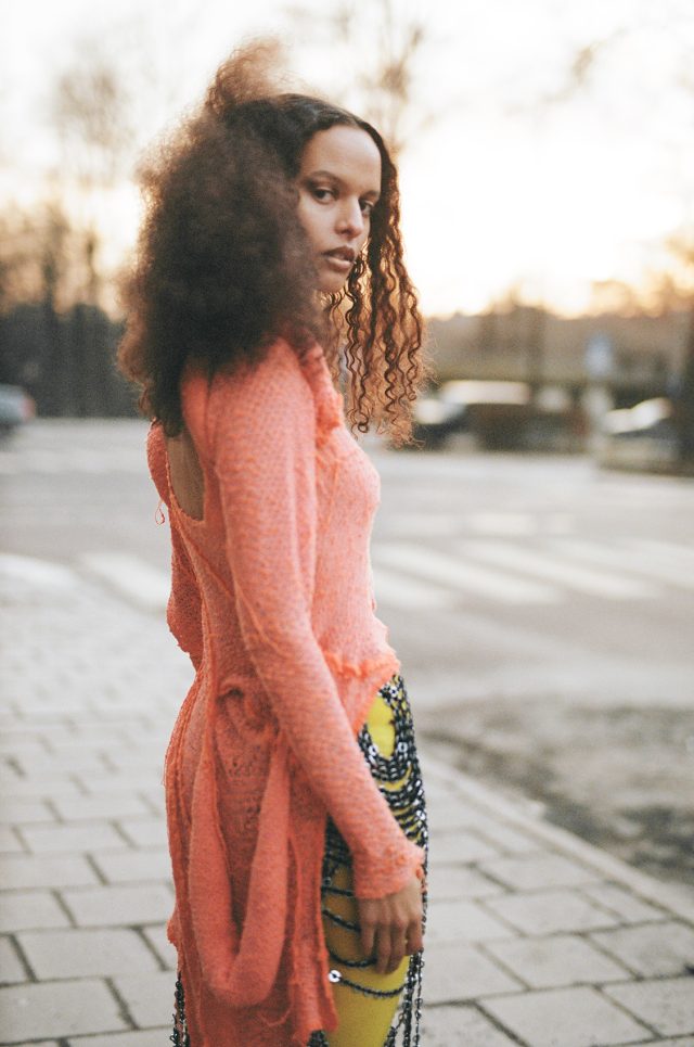 a woman with curly hair standing on a sidewalk