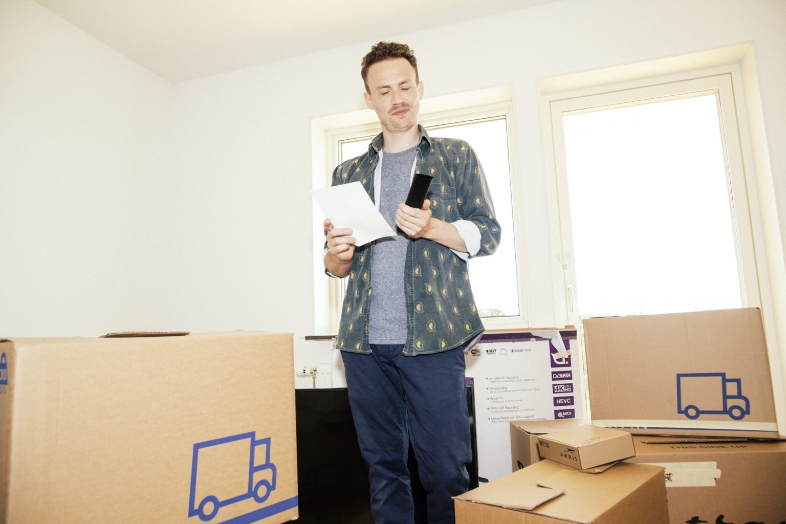a man standing in a room with boxes and a paper and phone
