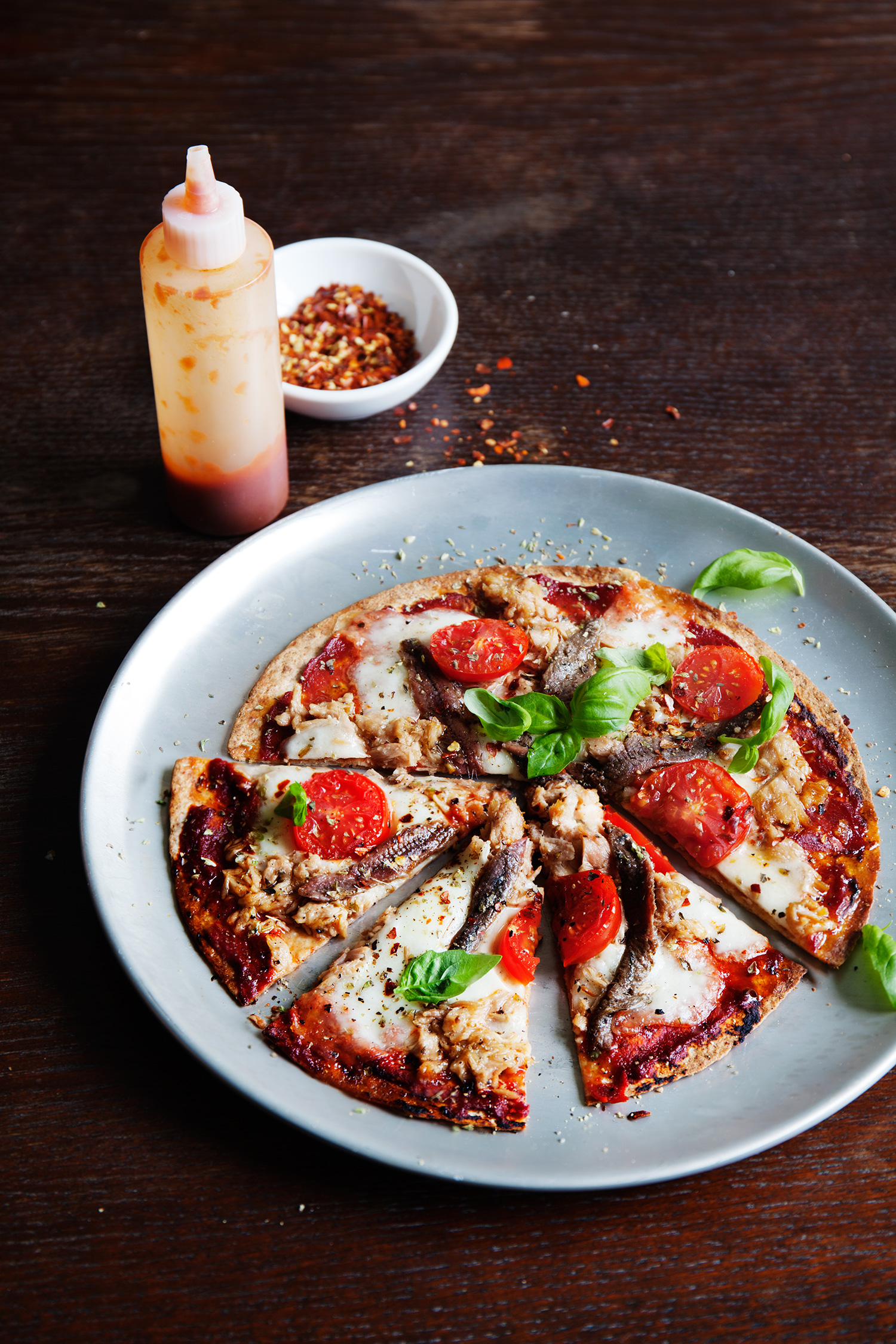 a pizza on a plate next to a bottle of sauce