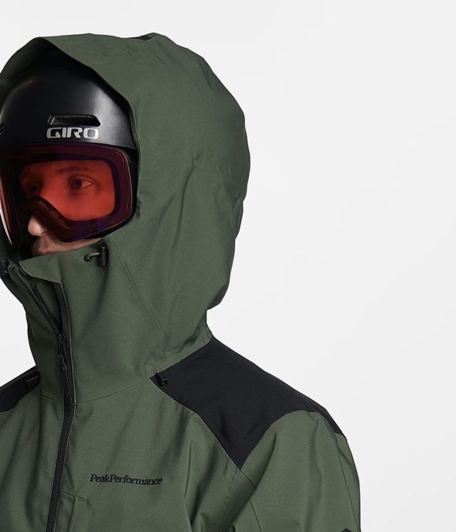 Person in green ski jacket, black helmet, and red goggles.