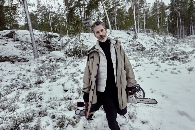 a man in a coat holding a chainsaw in a snowy forest