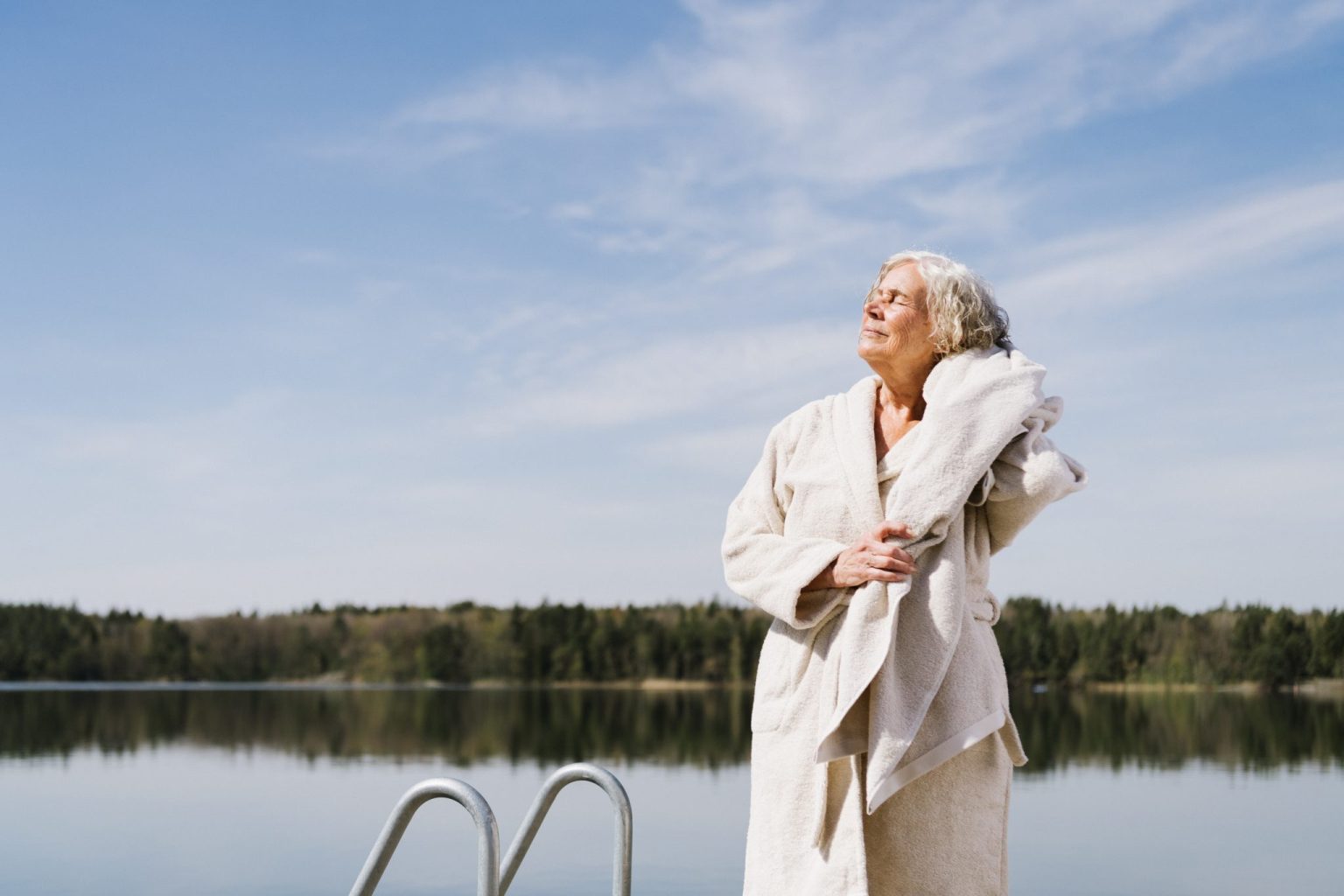 a woman in a bathrobe standing on a dock near water