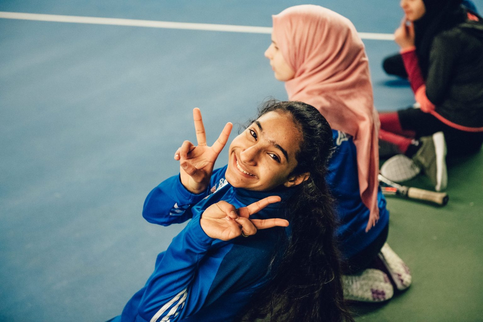 a girl sitting on the ground with a woman holding up a peace sign
