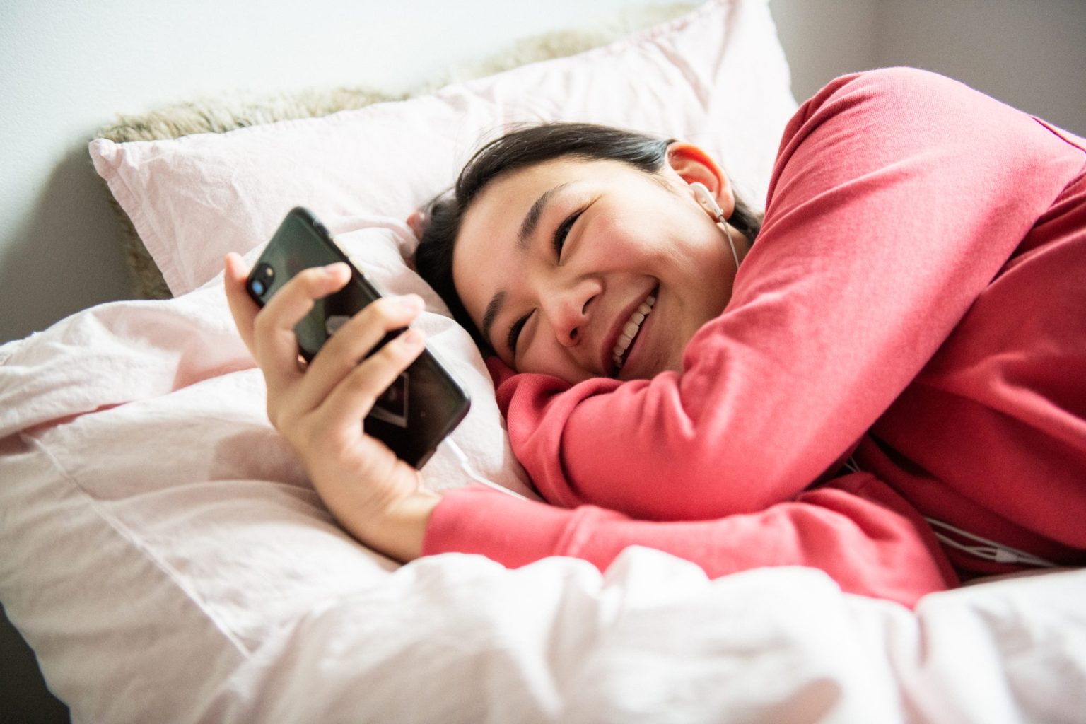 a woman lying in bed holding a phone