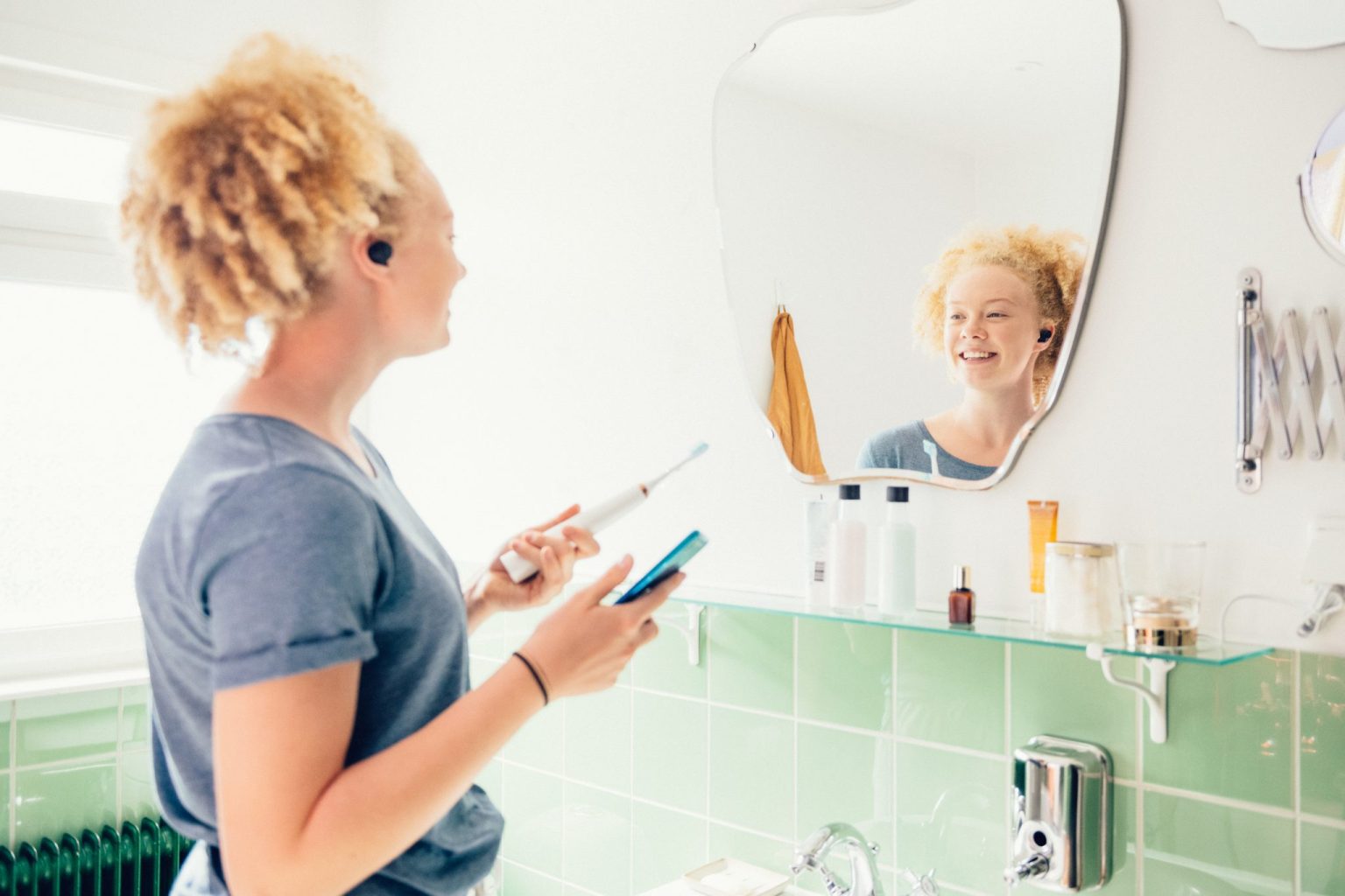 a woman holding a toothbrush and looking at a mirror