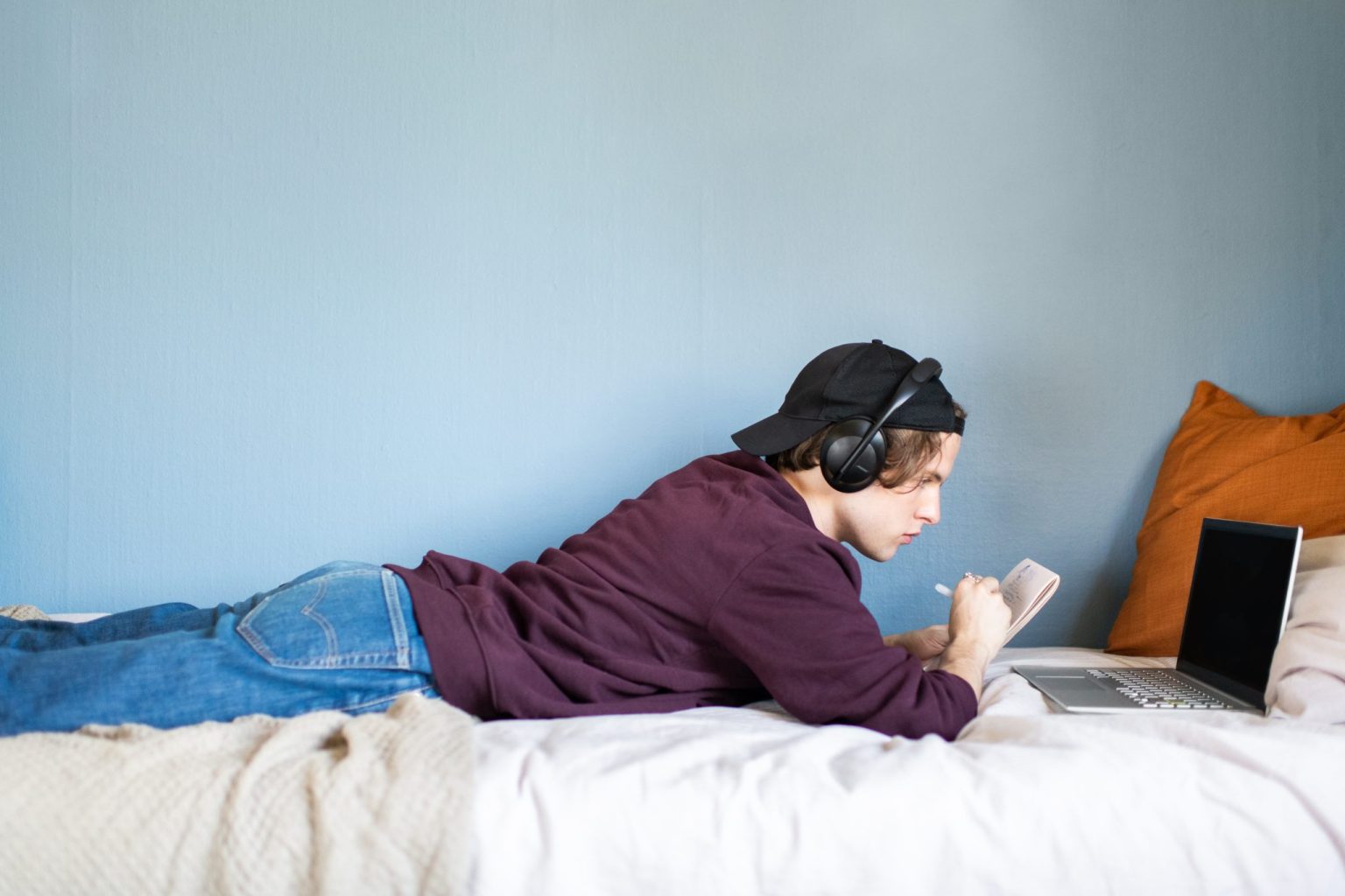 a man lying on a bed with a laptop and headphones