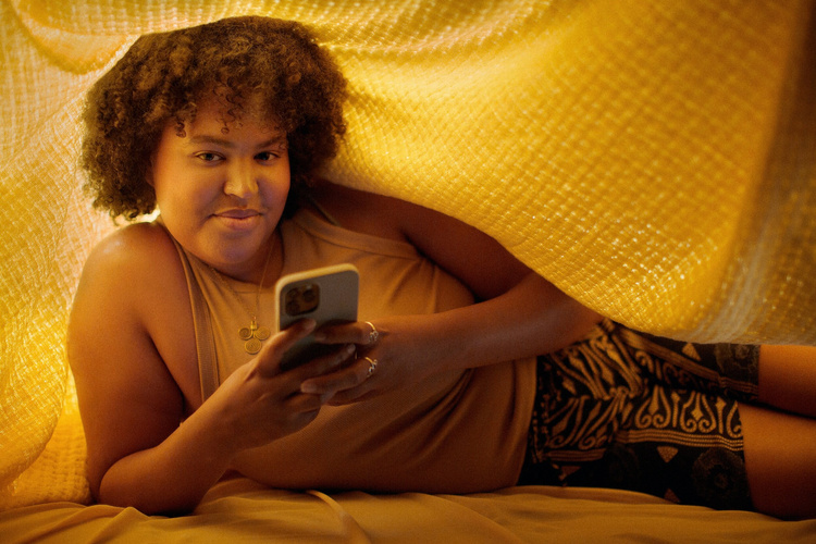 a woman lying under a blanket holding a phone