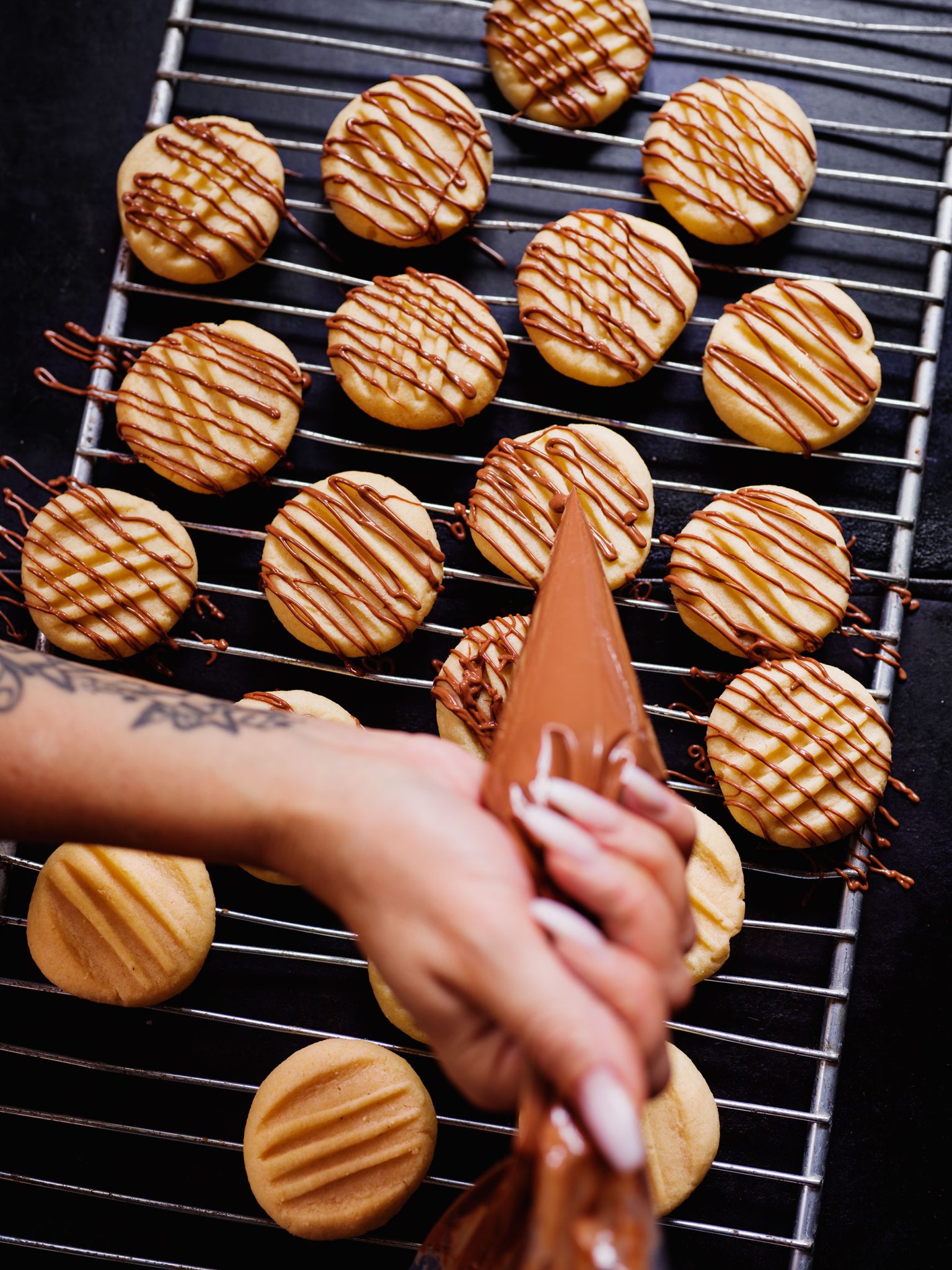 a hand holding a pastry bag over cookies
