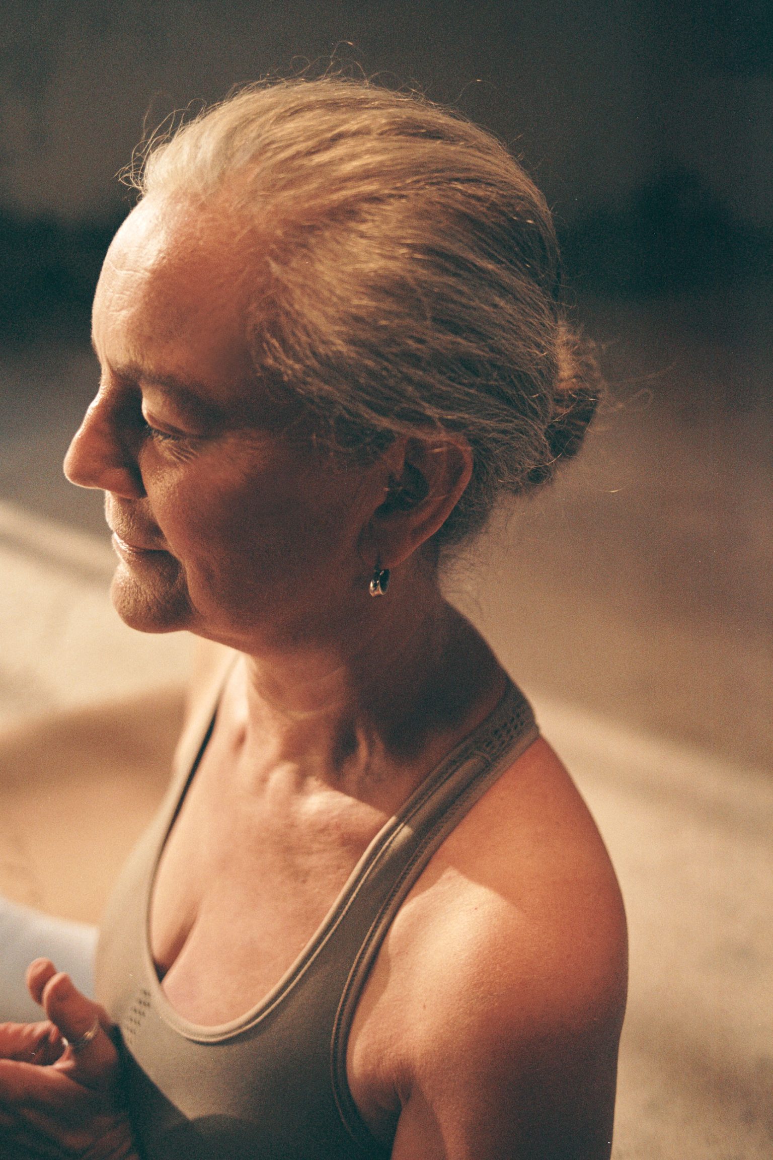 Close-up of an older woman with gray hair pulled back, wearing a gray tank top.