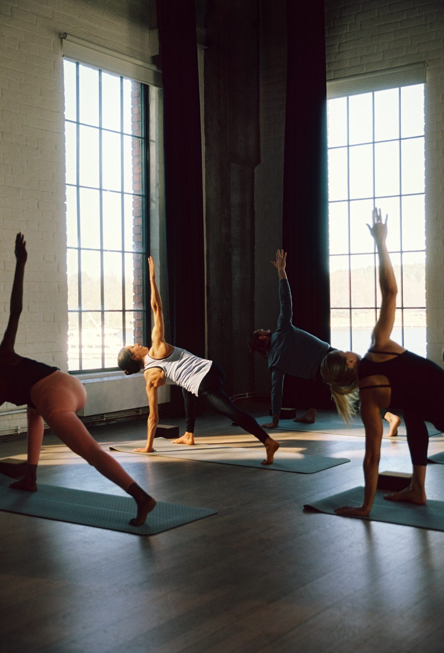 People practicing yoga in a bright room with large windows.