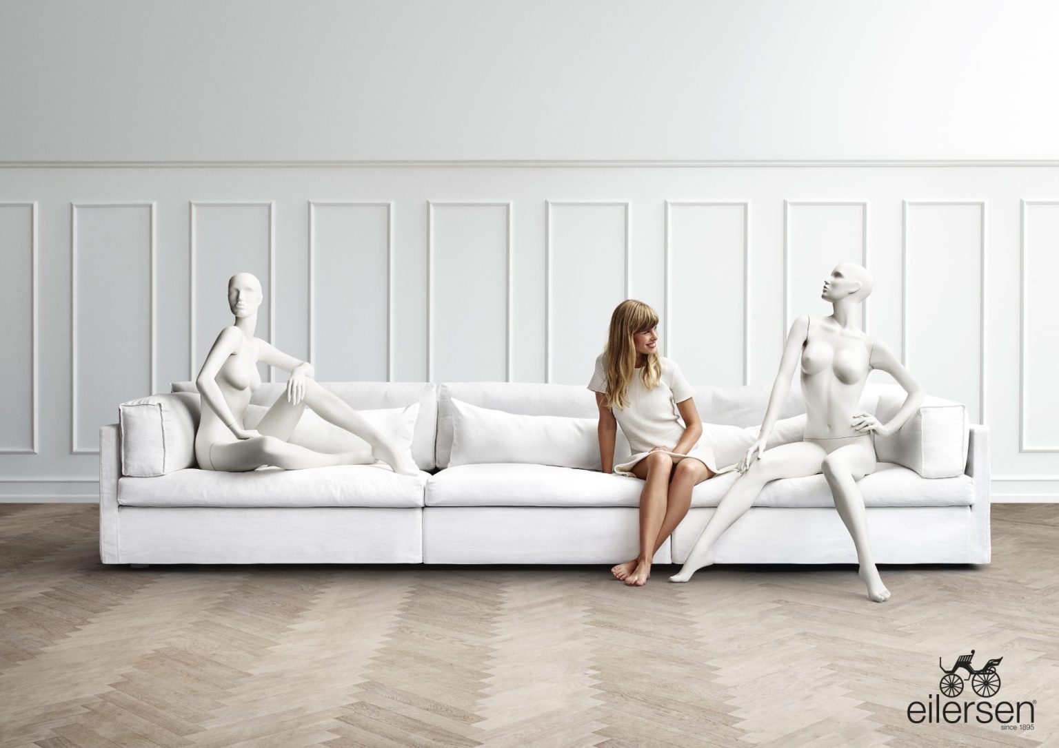 a woman sitting on a couch with several mannequins