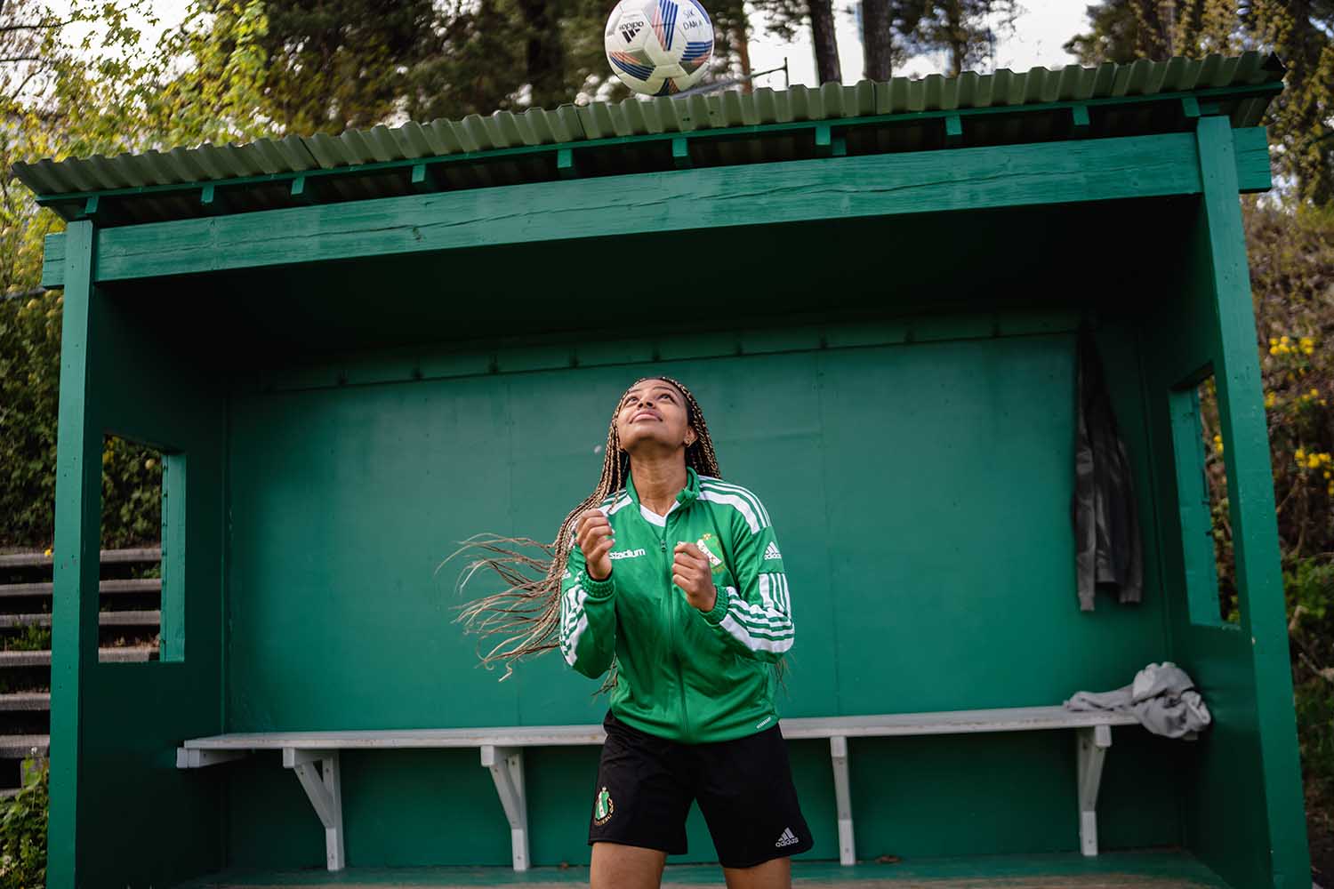 a woman in a green jacket and black shorts with a football ball in the air