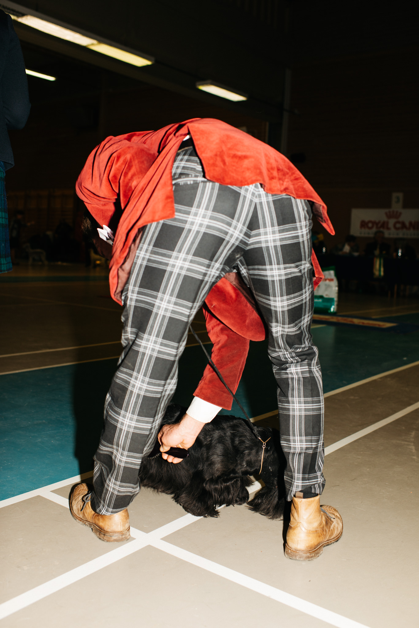 a person in a red coat and plaid pants bending over a dog