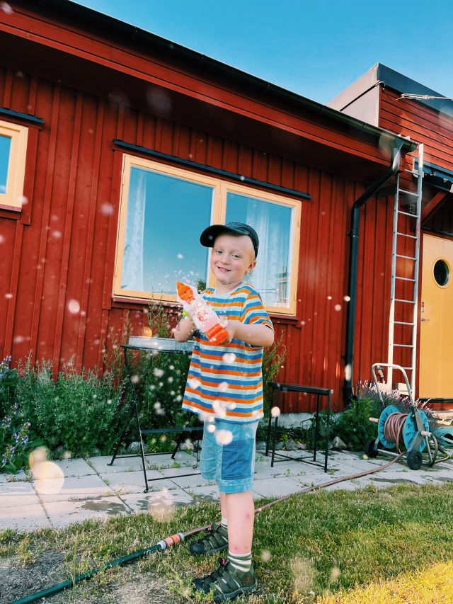 a boy standing in the grass with a toy gun in front of a red house