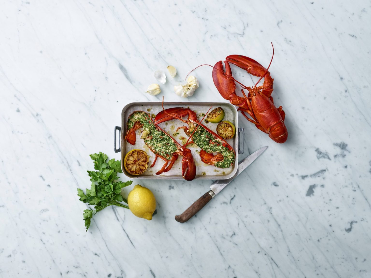 a lobsters on a pan next to a knife and lemon